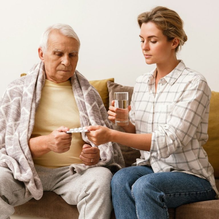 Maatje Dichtbij helpt een man terwijl hij op de bank zit, onder een deken.