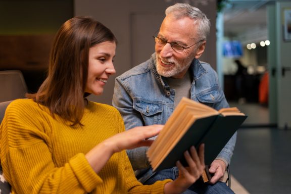 Een jongeman en een oudere man kijken samen naar een boek, met een vriendelijke interactie.