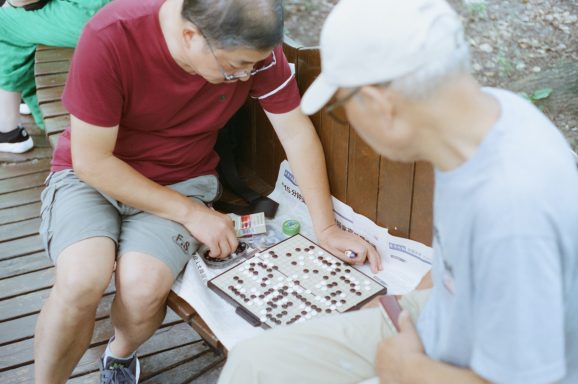 Twee mannen spelen een bordspel op een bank in een park.