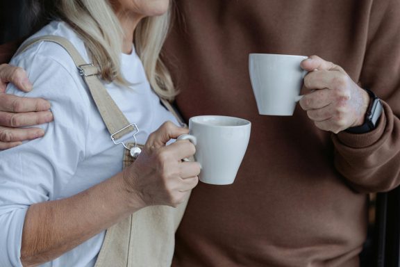 Een oudere vrouw en man houden mokken vast en staan dicht bij elkaar.