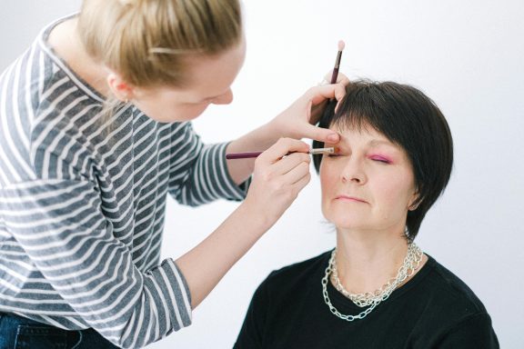 Een visagist maakt make-up aan voor een vrouw met kort haar.