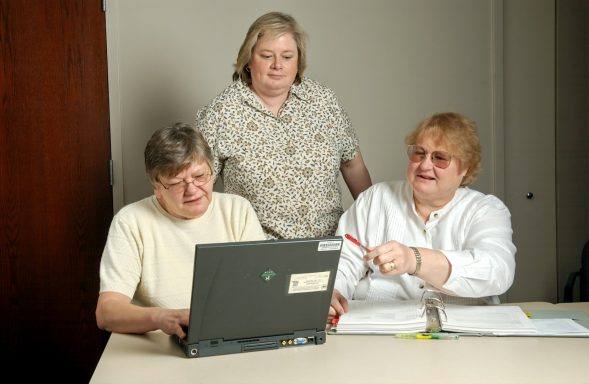 Drie vrouwen werken samen aan een laptop en bespreken documenten.